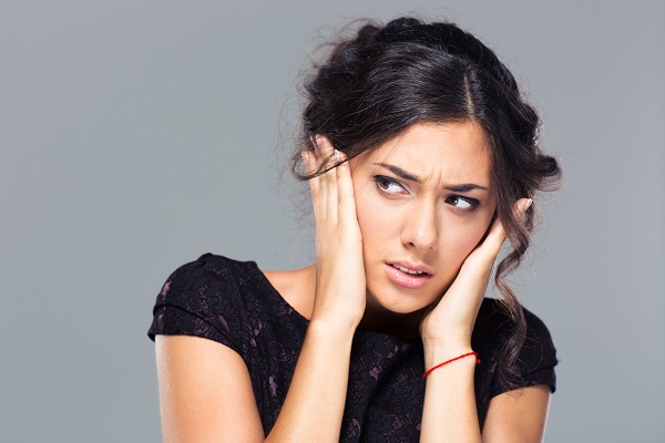 Portrait of a beautiful woman covering her ears on grary background